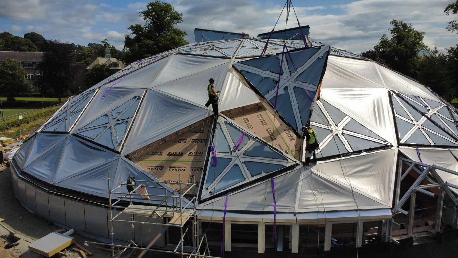 Rope access technicians guiding a crane-lifted ETFE panel onto a geodesic dome roof