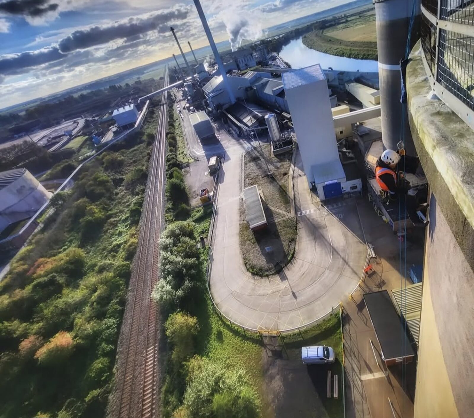Rope access technician descending an industrial chimney high above a railway line